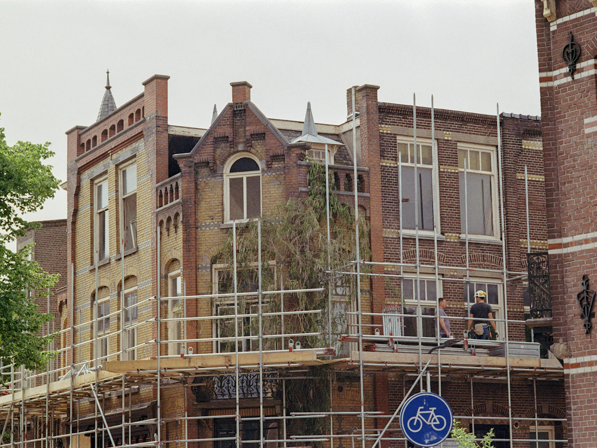Bakstenen herenhuis in de stellingen tijdens een renovatie, met een fietsbord op de voorgrond